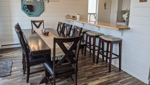 A dining area with a wooden table, dark chairs, a chandelier, and a kitchen counter.