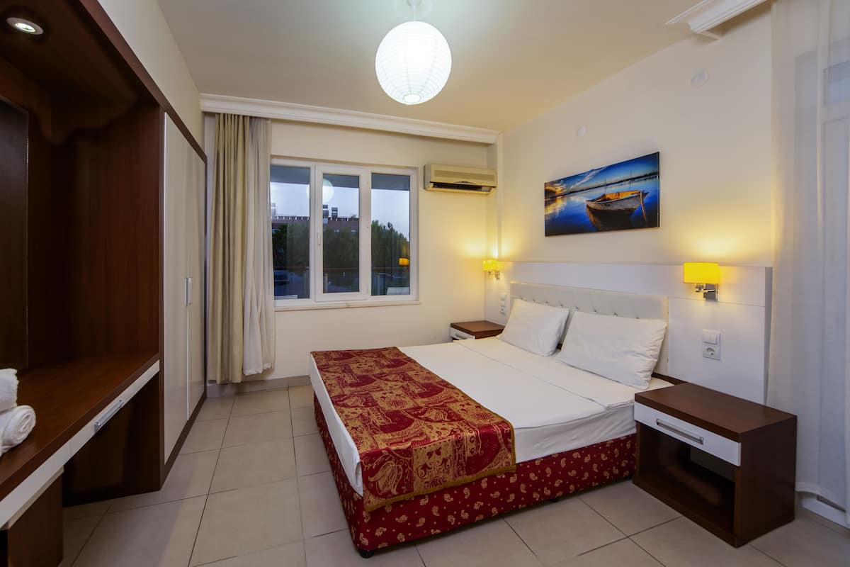 A hotel room with a bed, bedside tables, a window, and a painting on the wall.
