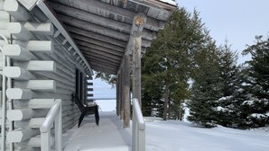 A wooden cabin with a snow-covered porch and a view of the forest. - UP LIVING on Big Manistique Lake at its finest. 200 ft of private lake frontage. (Curtis)
