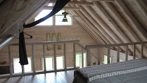 A wooden attic bedroom with a sloped ceiling, a bed, and a window with curtains. - UP LIVING on Big Manistique Lake at its finest. 200 ft of private lake frontage. (Curtis)