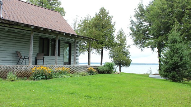 A cabin with a porch, chairs, and a view of a lake. - UP LIVING on Big Manistique Lake at its finest. 200 ft of private lake frontage. (Curtis)