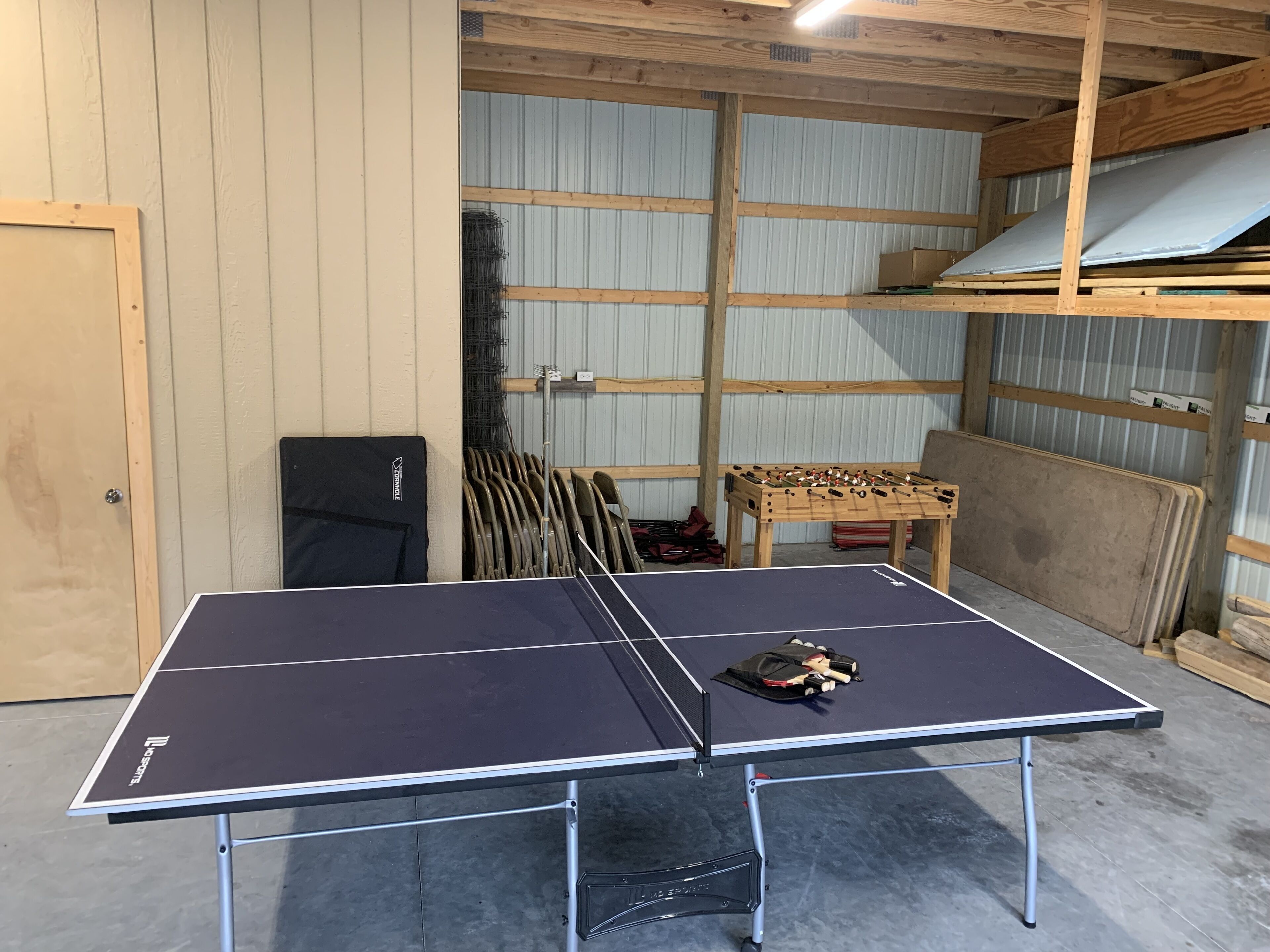 Ett bordtennisbord i ett rum med träväggar och en metalldörr.