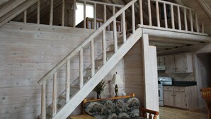A wooden staircase leading to an upper level in a cabin-style room with a kitchen area visible below. - UP LIVING on Big Manistique Lake at its finest. 200 ft of private lake frontage. (Curtis)