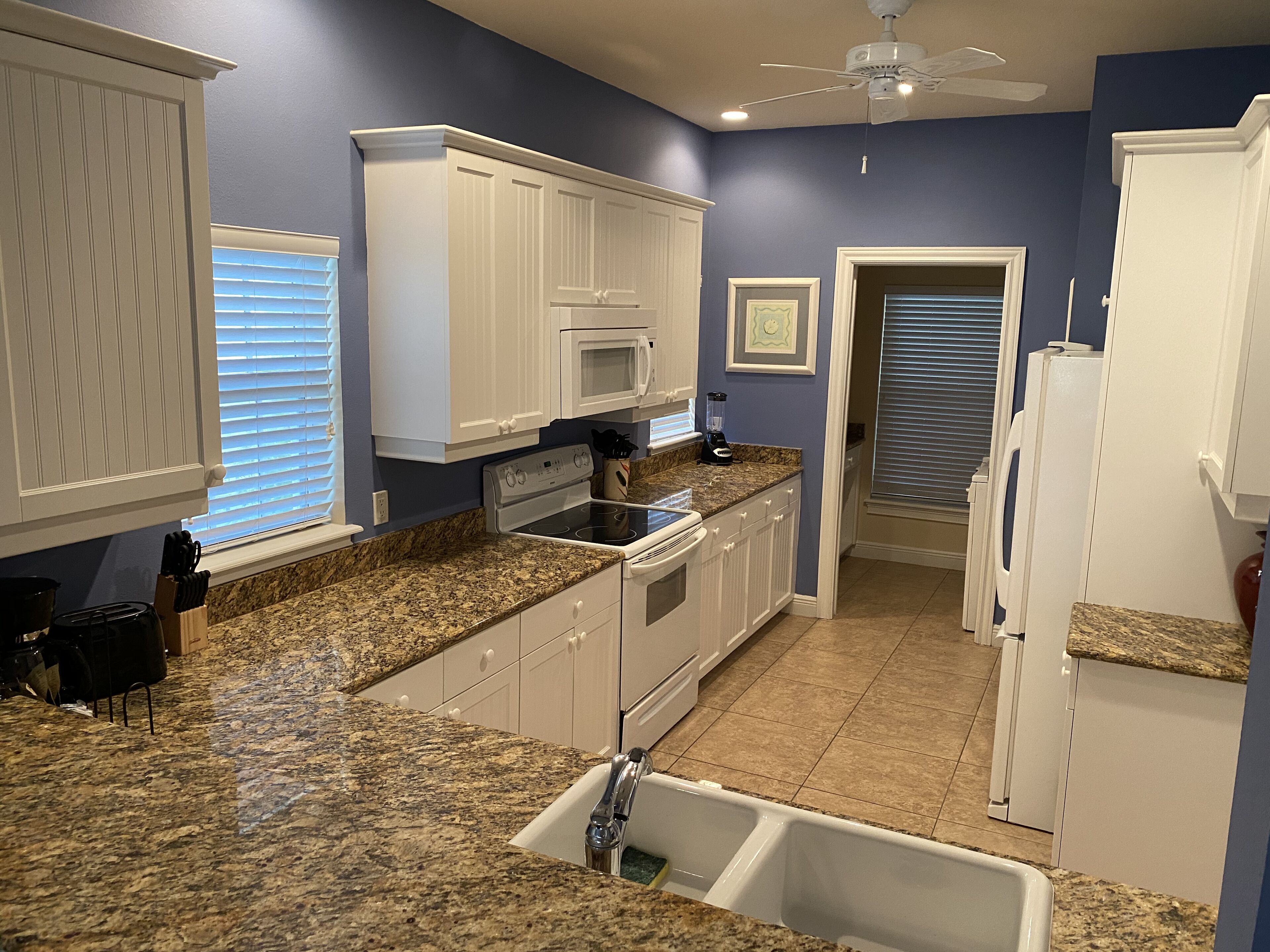 A kitchen with granite countertops, white cabinets, a microwave, a stove, and a ceiling fan.