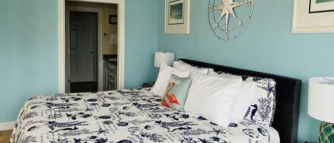 A bedroom with a bed, a nightstand, a wall clock, and a door leading to a bathroom.