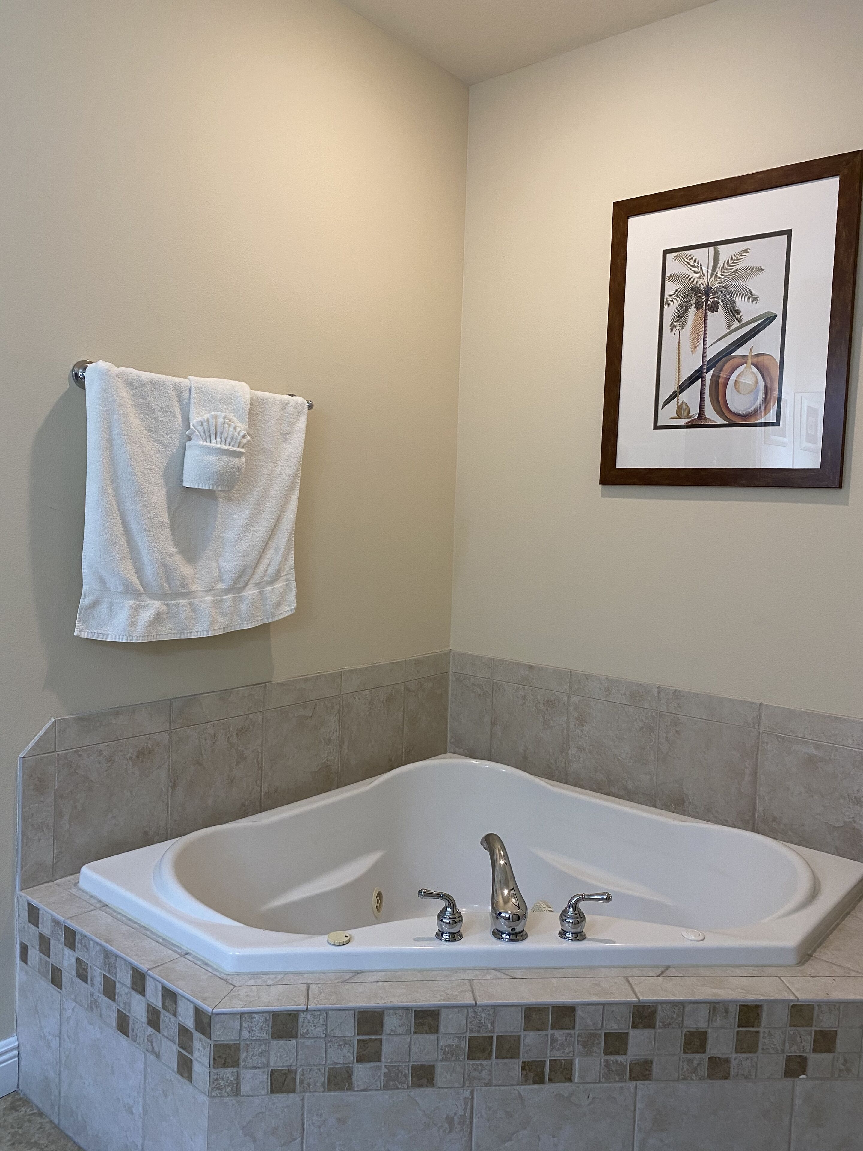 A bathroom with a large bathtub, a towel hanging on the wall, and a framed picture above the bathtub.