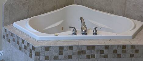 A bathroom with a large bathtub, a towel hanging on the wall, and a framed picture above the bathtub.