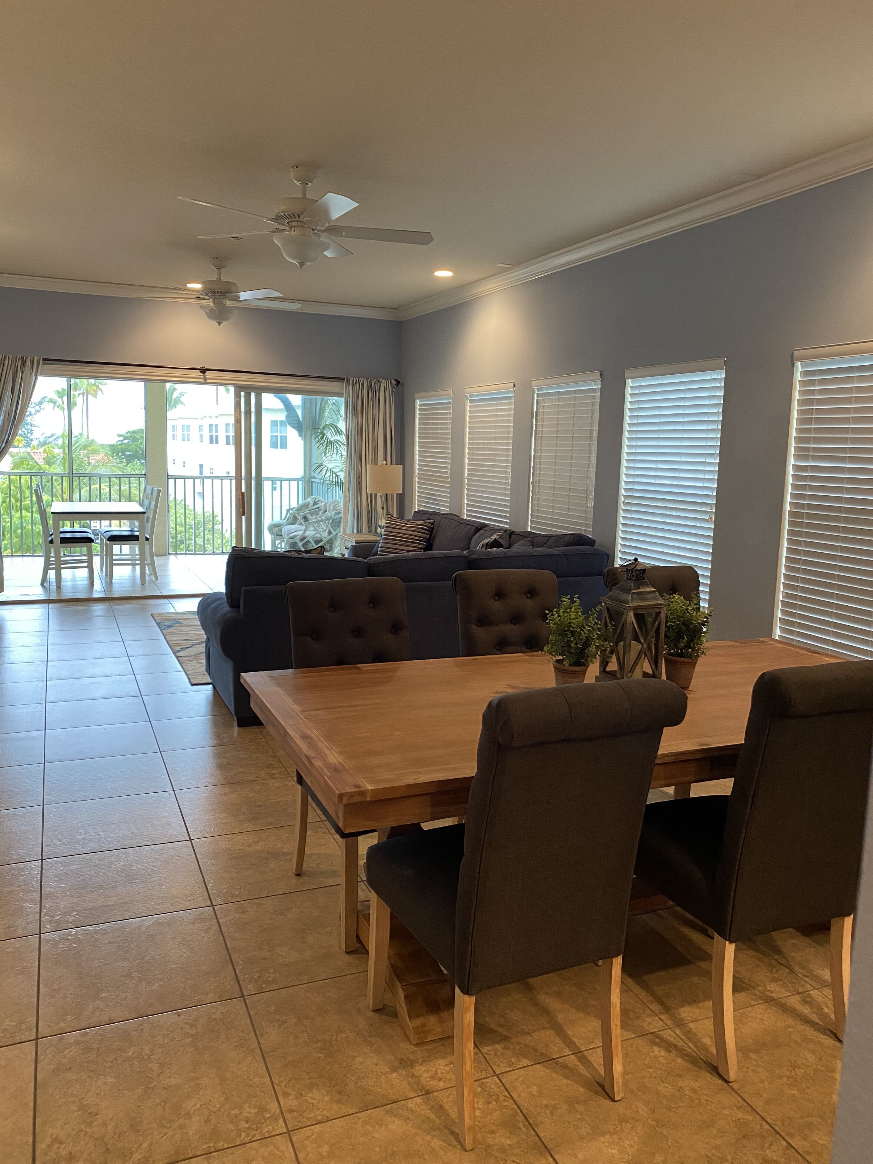 A spacious living area with a dark-colored sofa, a wooden dining table, and a ceiling fan.