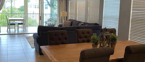 A spacious living area with a dark-colored sofa, a wooden dining table, and a ceiling fan.