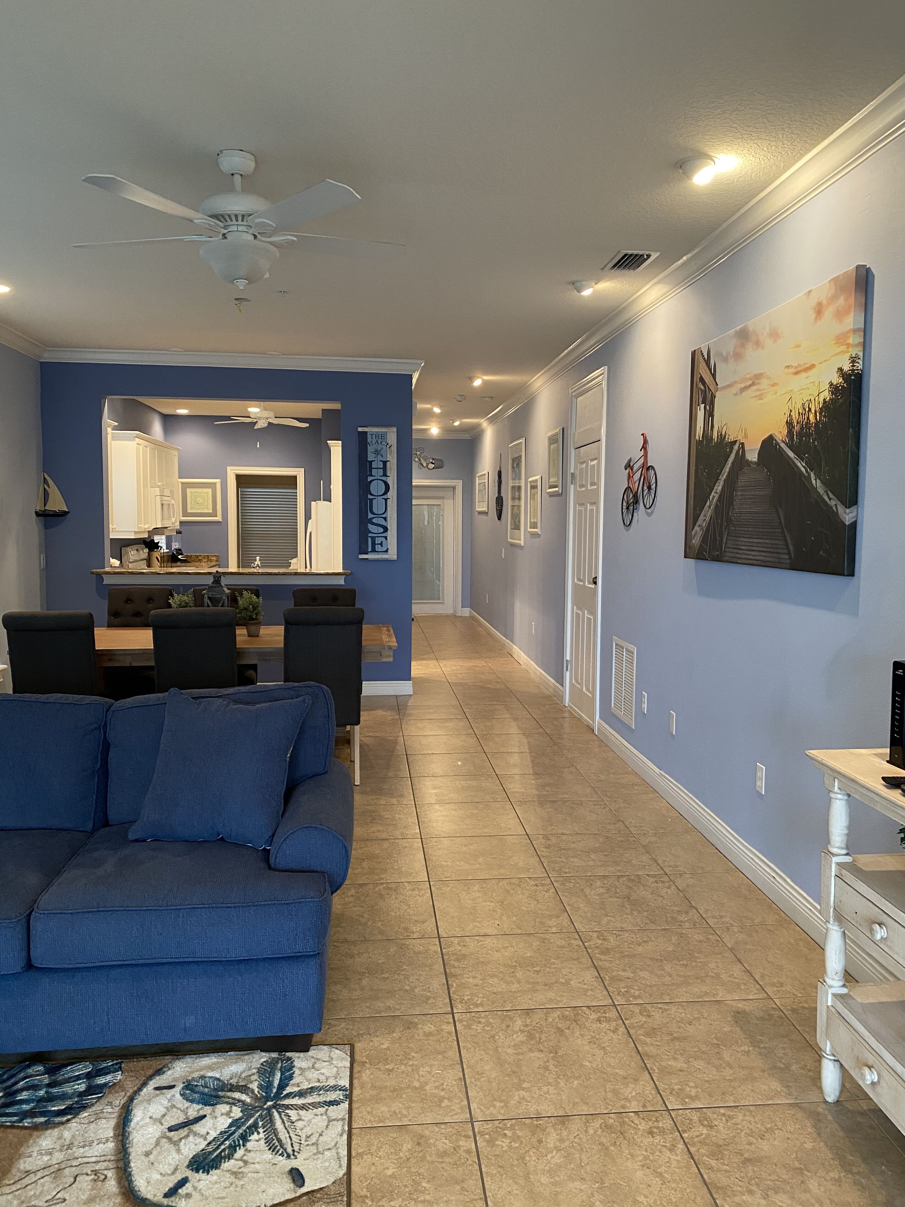 A spacious living area with a blue sofa, a dining table, and a kitchen area with cabinets and a refrigerator.