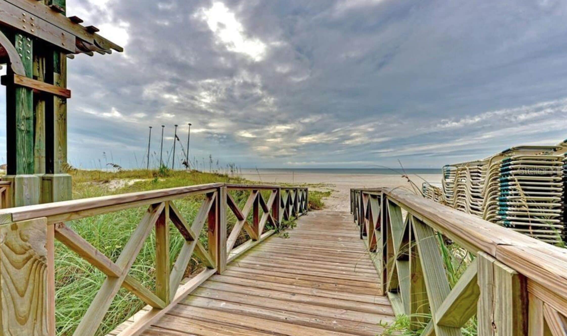 Une promenade en bois menant à une plage, avec un ciel nuageux.