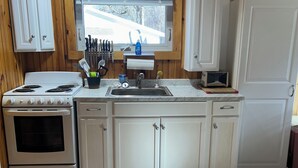 A kitchen with wooden walls, a stove, a sink, and cabinets.