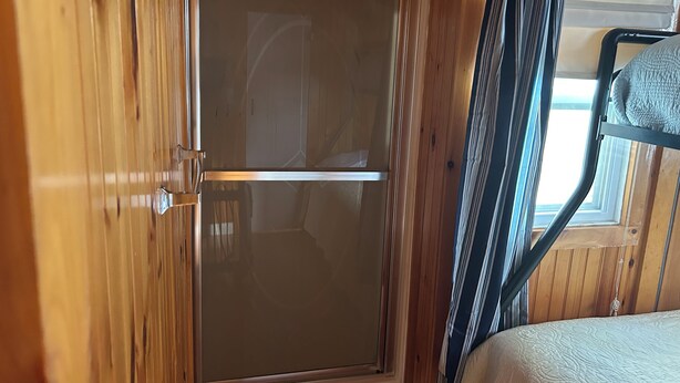 A wooden door with a frosted glass panel, a bunk bed with a white mattress, and a window with curtains.
