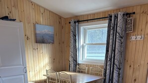 A cozy room with a wooden interior, a dining table with chairs, a white refrigerator, and a window with curtains.