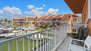 A balcony with white wicker furniture, a marina with boats, and a row of colorful buildings with balconies.
