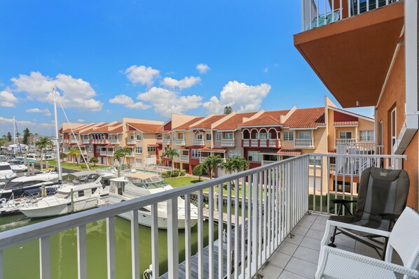 Ein Balkon mit weißen Korbmöbeln, eine Marina mit Booten und eine Reihe farbenfroher Gebäude mit Balkonen.