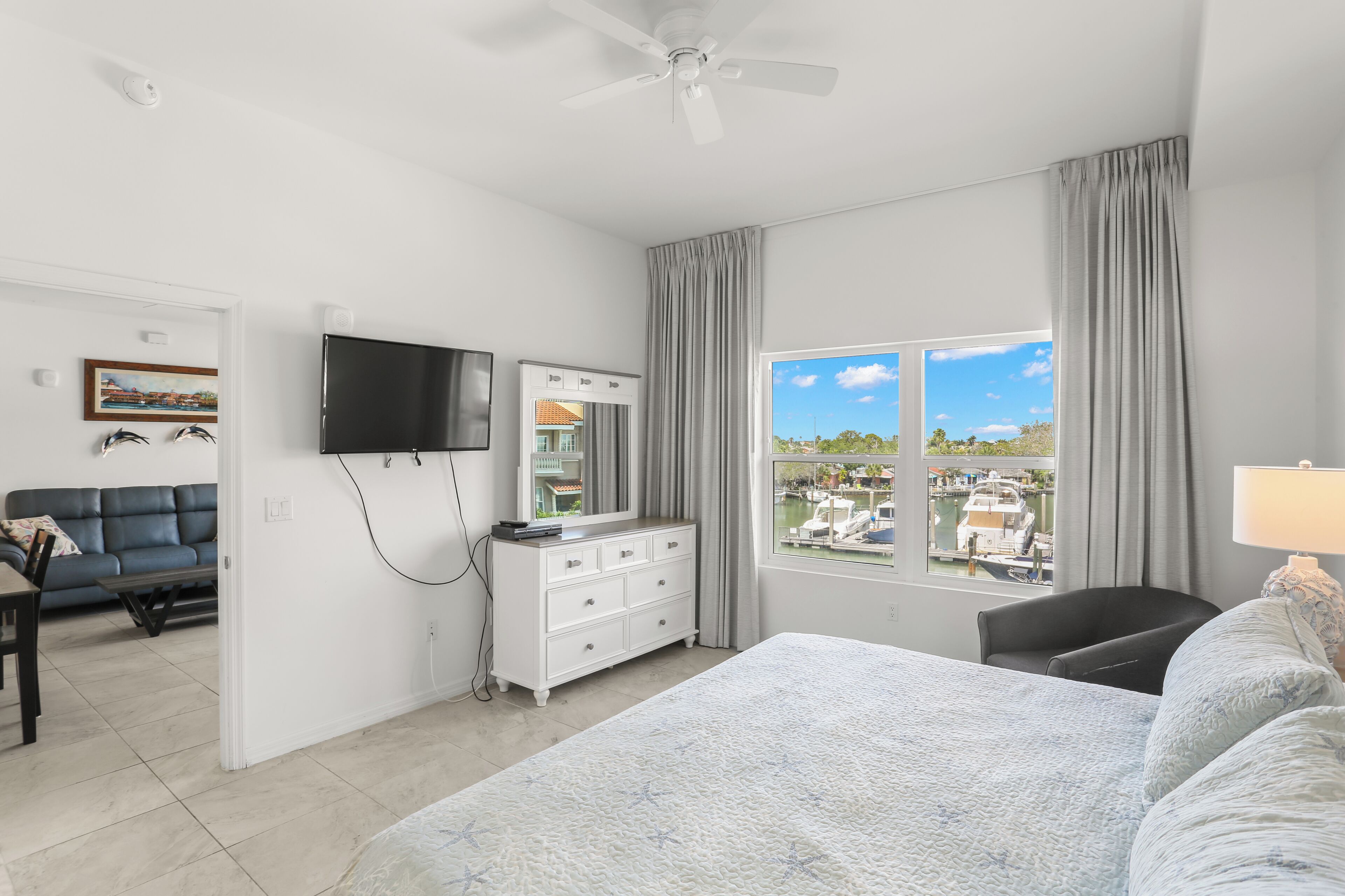 A hotel room with a bed, a TV, a dresser, and a window with a view of a marina.