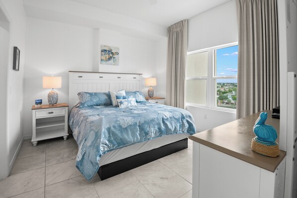 A bedroom with a bed, two bedside tables, a window with curtains, and a view of the outside. - đž Madeira Bay Resort I #1601 â Spacious, Pet-Friendly Escape by the Shore (Madeira Beach)