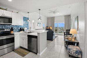 A modern kitchen with white cabinets, a built-in microwave, and a dishwasher. There is a dining area with a sofa and a table, and a balcony with a view. - đž Madeira Bay Resort I #1601 â Spacious, Pet-Friendly Escape by the Shore (Madeira Beach)