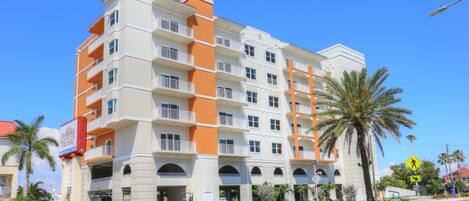 A multi-story hotel with balconies, a pedestrian crossing sign, and a palm tree.