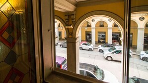 A view through a window with stained glass, revealing an outdoor area with parked cars and a building with arches. - GuestHost - ★ Apt in the very center! 500 meters from Porta Nuova ★ (Torino)