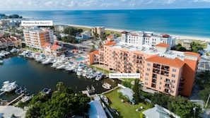 An aerial view of Madeira Bay Resort I and II, featuring multiple buildings with red roofs, a marina with boats, and a beach in the background.