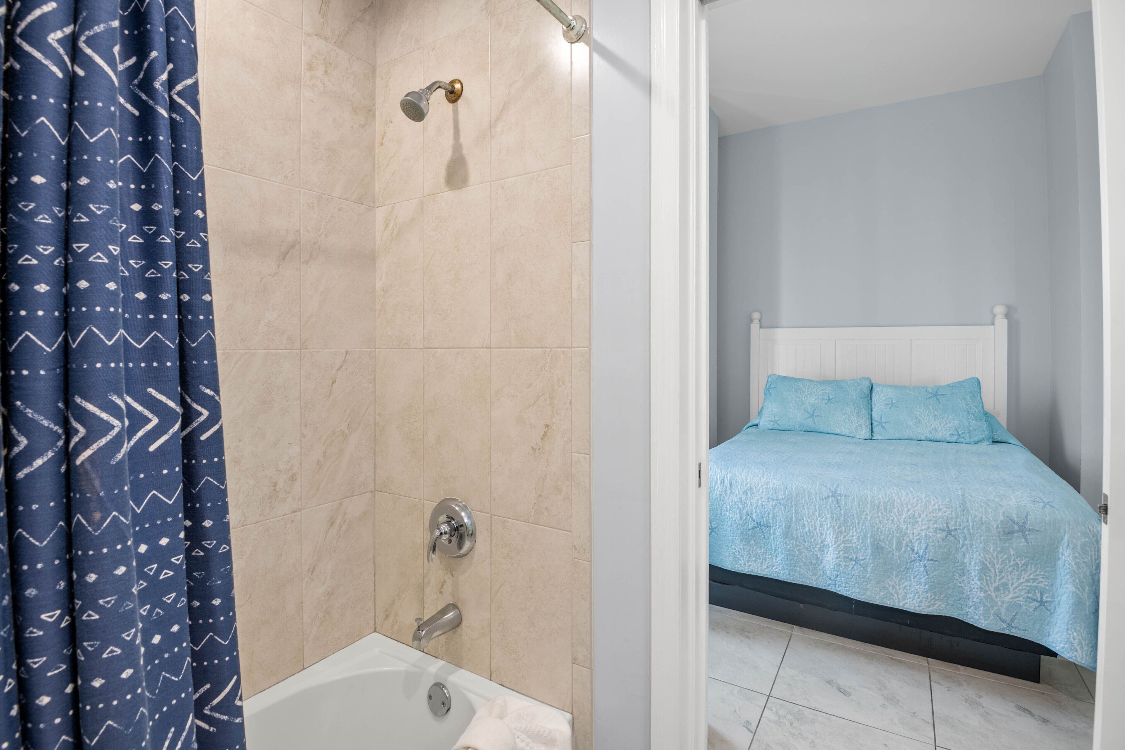 Un baño con ducha, bañera y una cama con cubrecama azul.