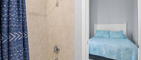 Un baño con ducha, bañera y una cama con cubrecama azul.