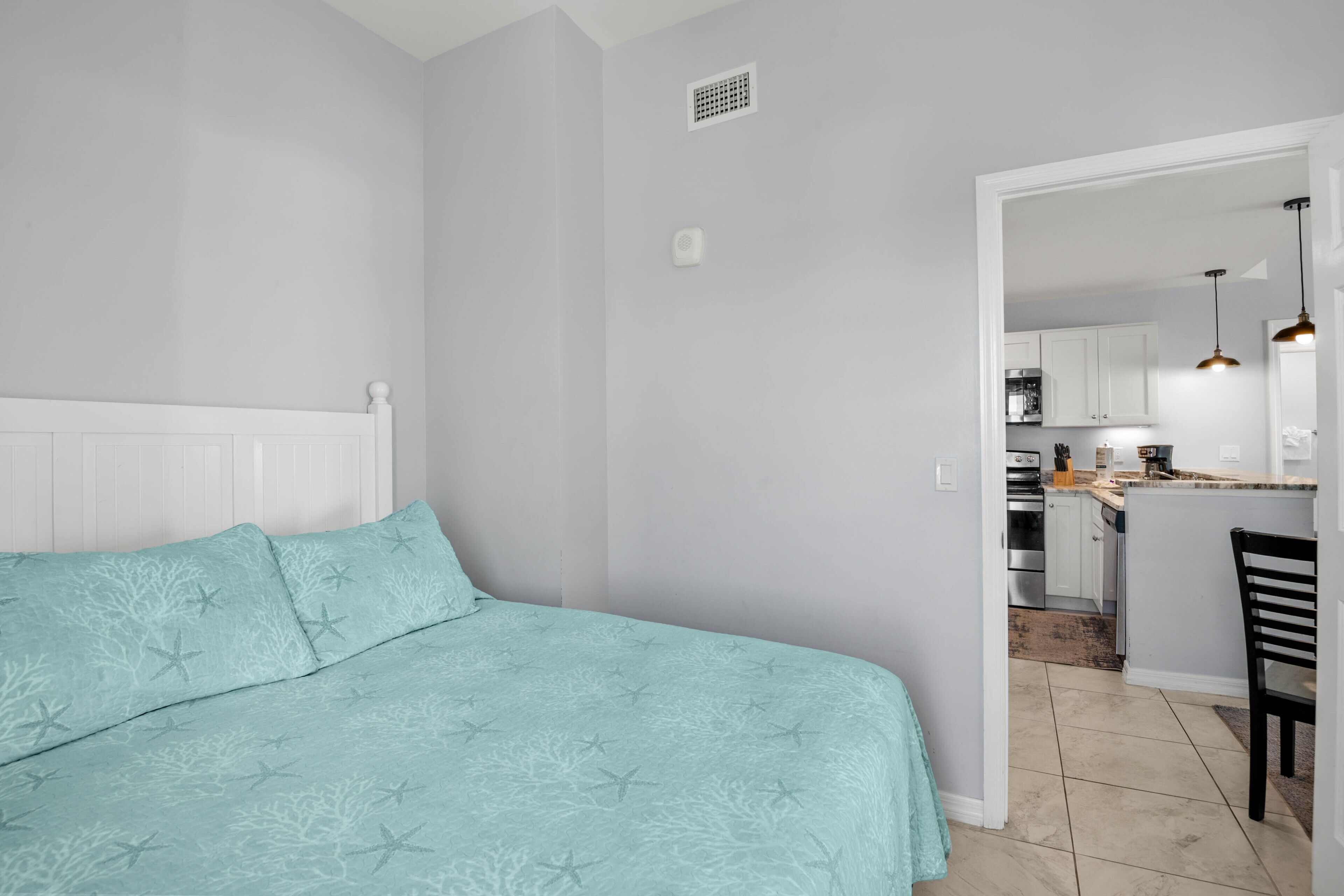 Un dormitorio con cama, una silla y vista a un área de cocina.