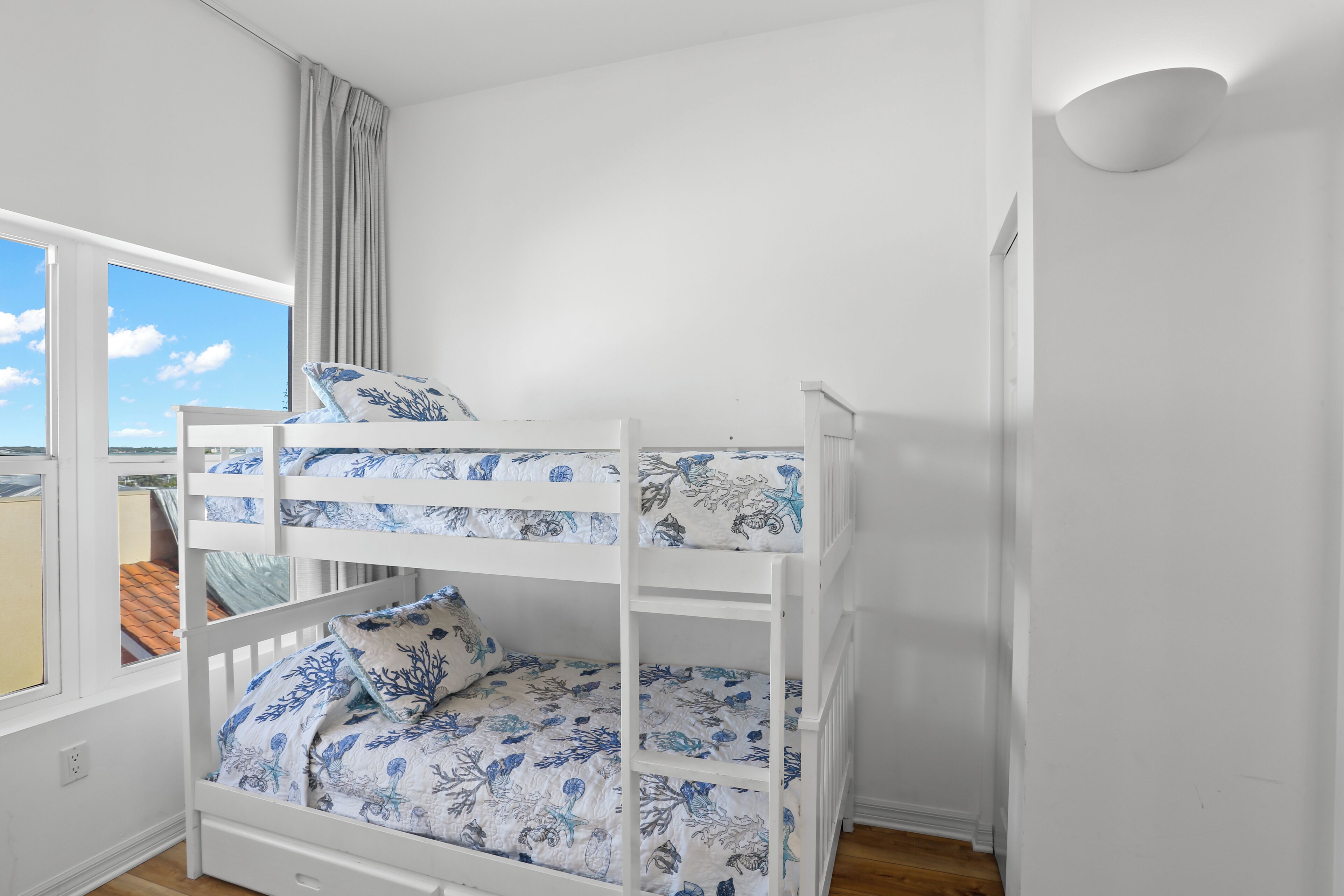 Ein Etagenbett mit Blumenmuster-Bettwäsche in einem Zimmer mit weißen Wänden und einem großen Fenster.