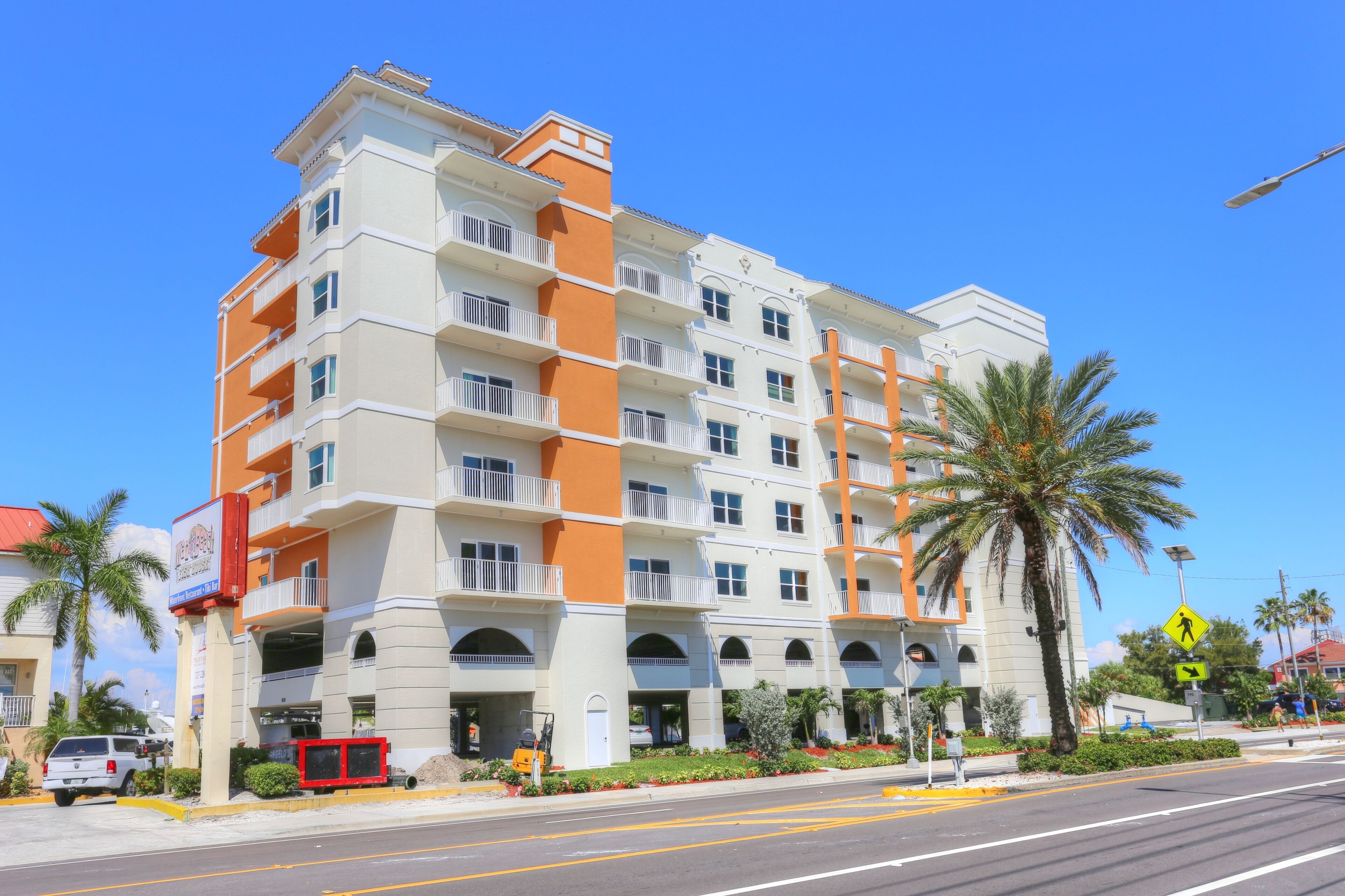 A multi-story hotel with balconies, a pedestrian crossing sign, and a palm tree.