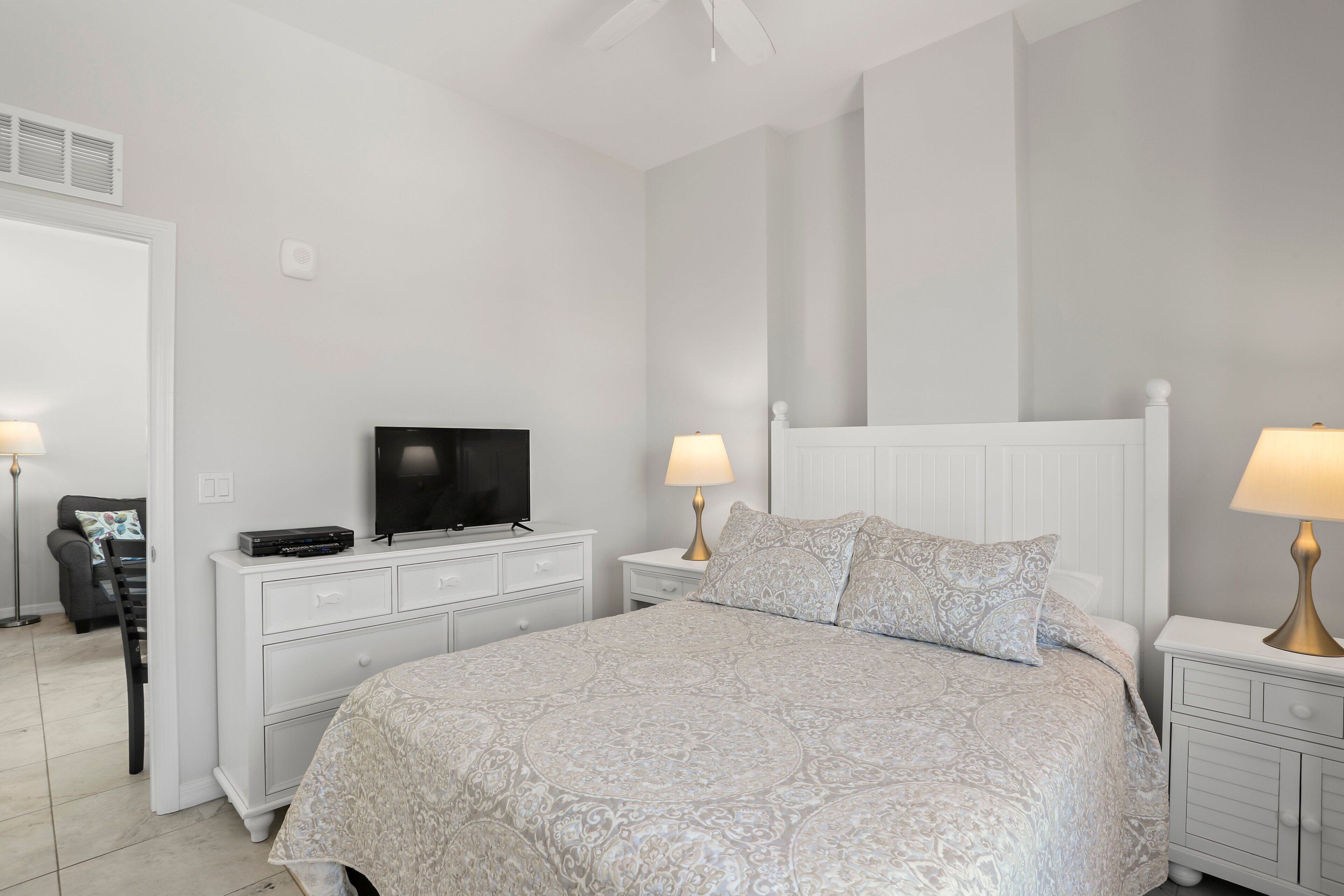 A bedroom with a bed, a TV, two bedside tables with lamps, a chair, and a dresser.