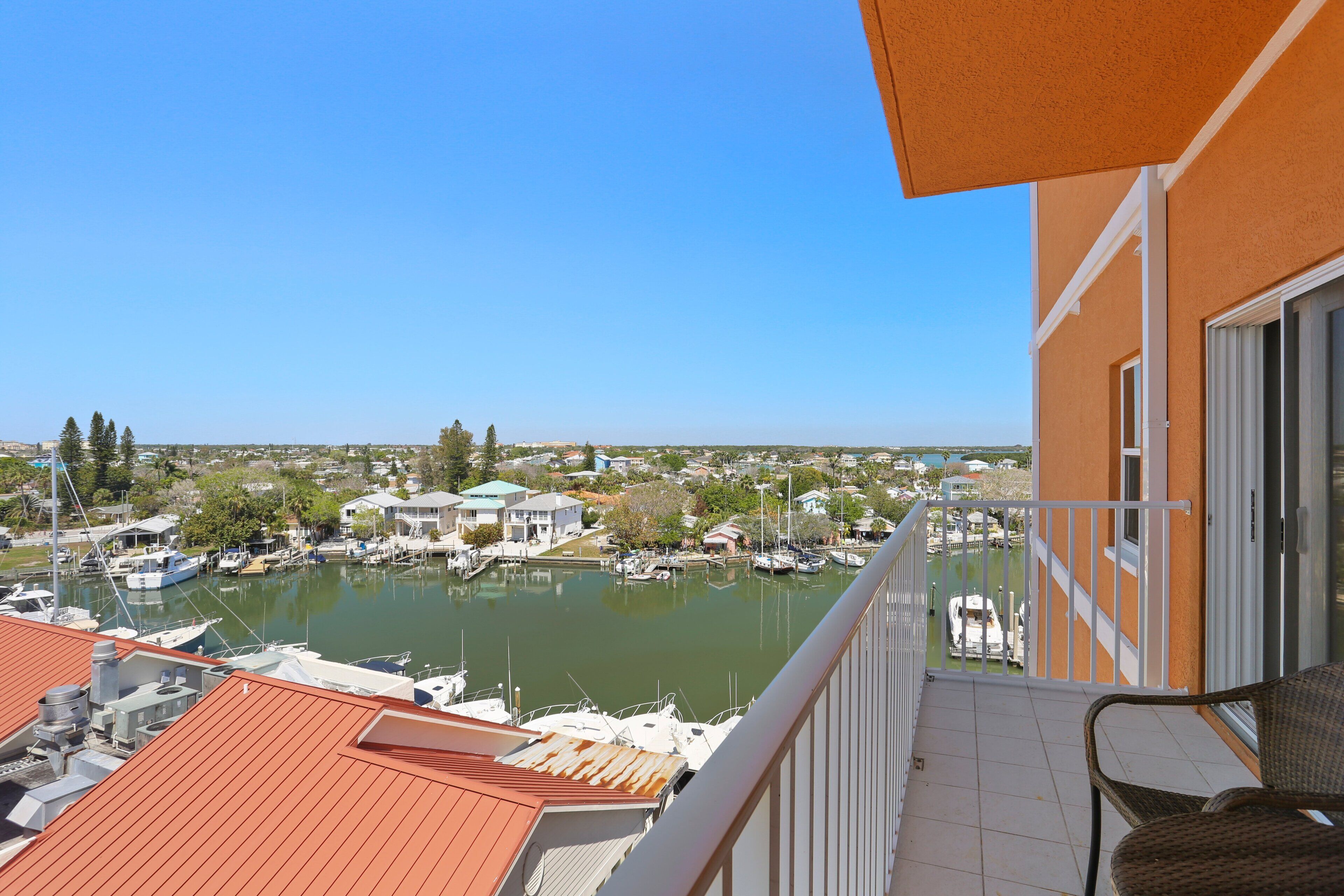 Een balkon met uitzicht op een jachthaven, boten en omliggende gebouwen.