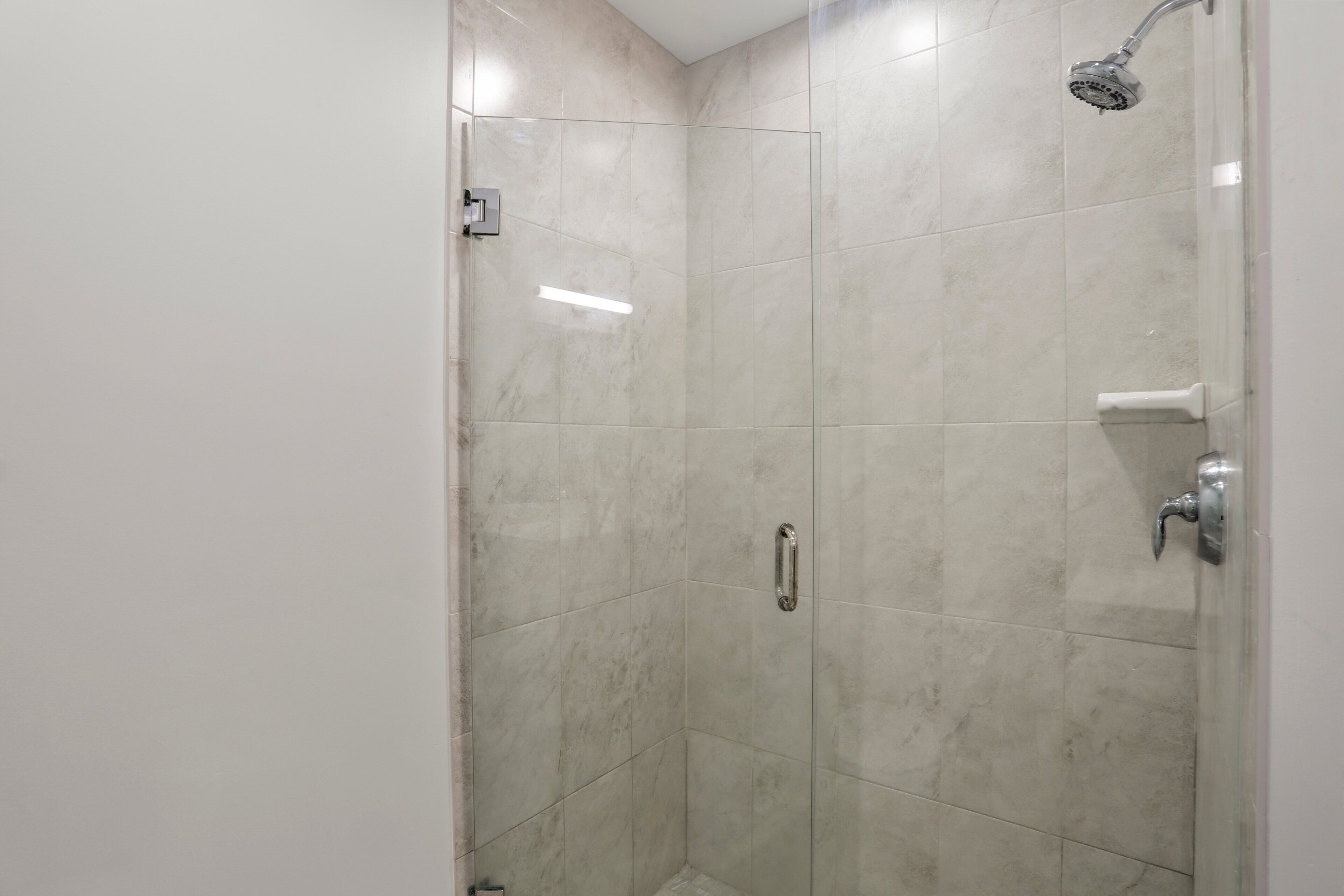 Une douche fermée par des parois en verre, dotée d’un pommeau de douche à main, d’un robinet mural et d’une porte avec une poignée.