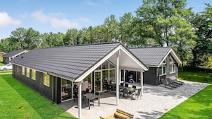 Ein modernes Haus mit überdachter Terrasse, großen Fenstern und einem gepflegten Rasen.