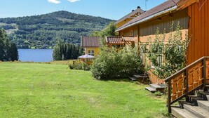 Une maison en bois avec un balcon, une cour verdoyante et un lac en arrière-plan.