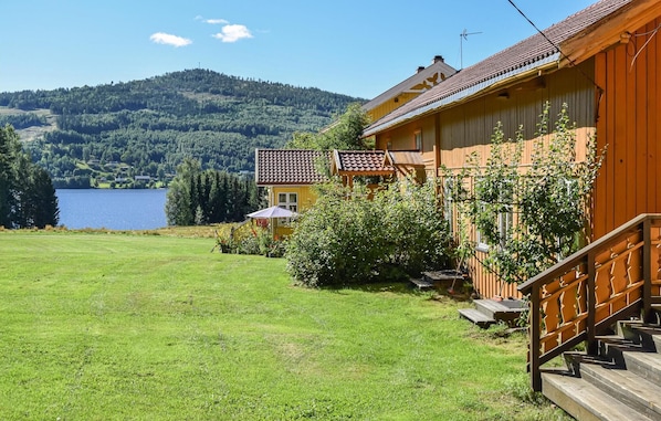 Una casa de madera con balcón, un patio con césped y un lago al fondo.