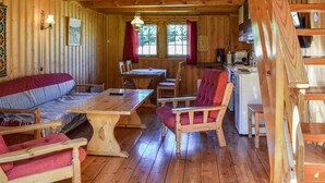 L’intérieur chaleureux d’un chalet comprend une table à manger en bois, des chaises à revêtement rouge, un canapé et un coin cuisine équipé d’un réfrigérateur et d’une cuisinière.