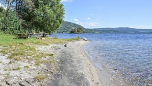 Un sentier au bord du lac, agrémenté d’une table de pique-nique et de bancs, entouré d’arbres et offrant une vue sur le lac et les collines lointaines.
