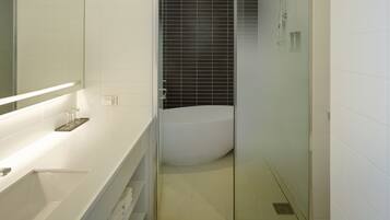 A modern bathroom with a white vanity, a large mirror, a glass shower enclosure, and black tiled walls.