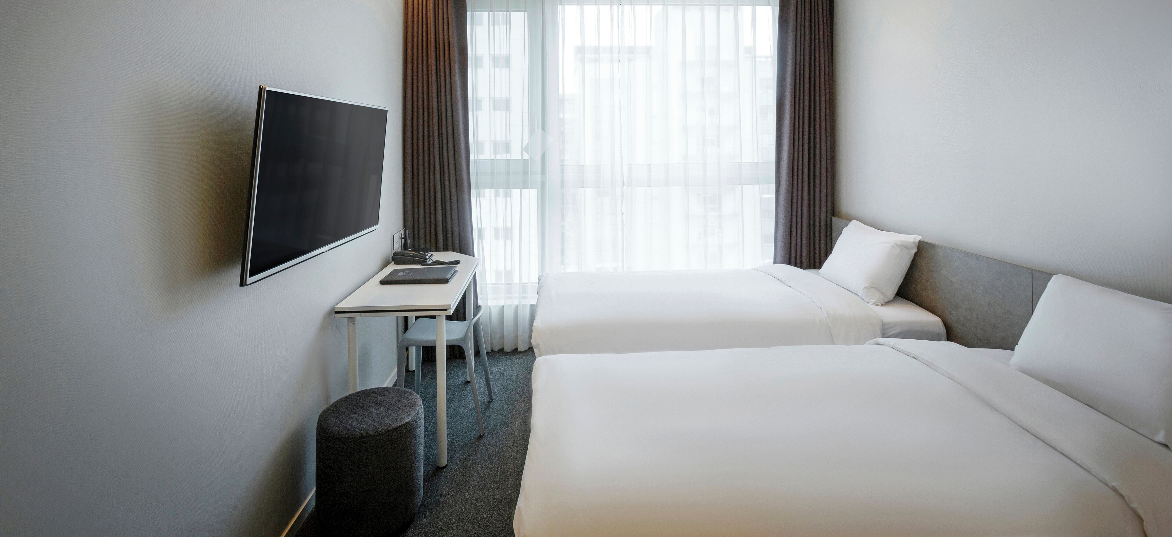 A hotel room with two beds, a TV, a desk, and a chair.