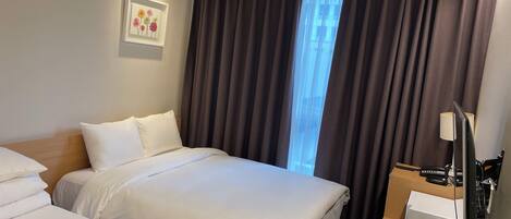 A hotel room with two beds, a desk with a lamp, a chair, and a window with curtains.
