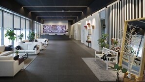 Un moderno vestíbulo de hotel con sofás blancos, un mostrador de recepción y grandes ventanales.