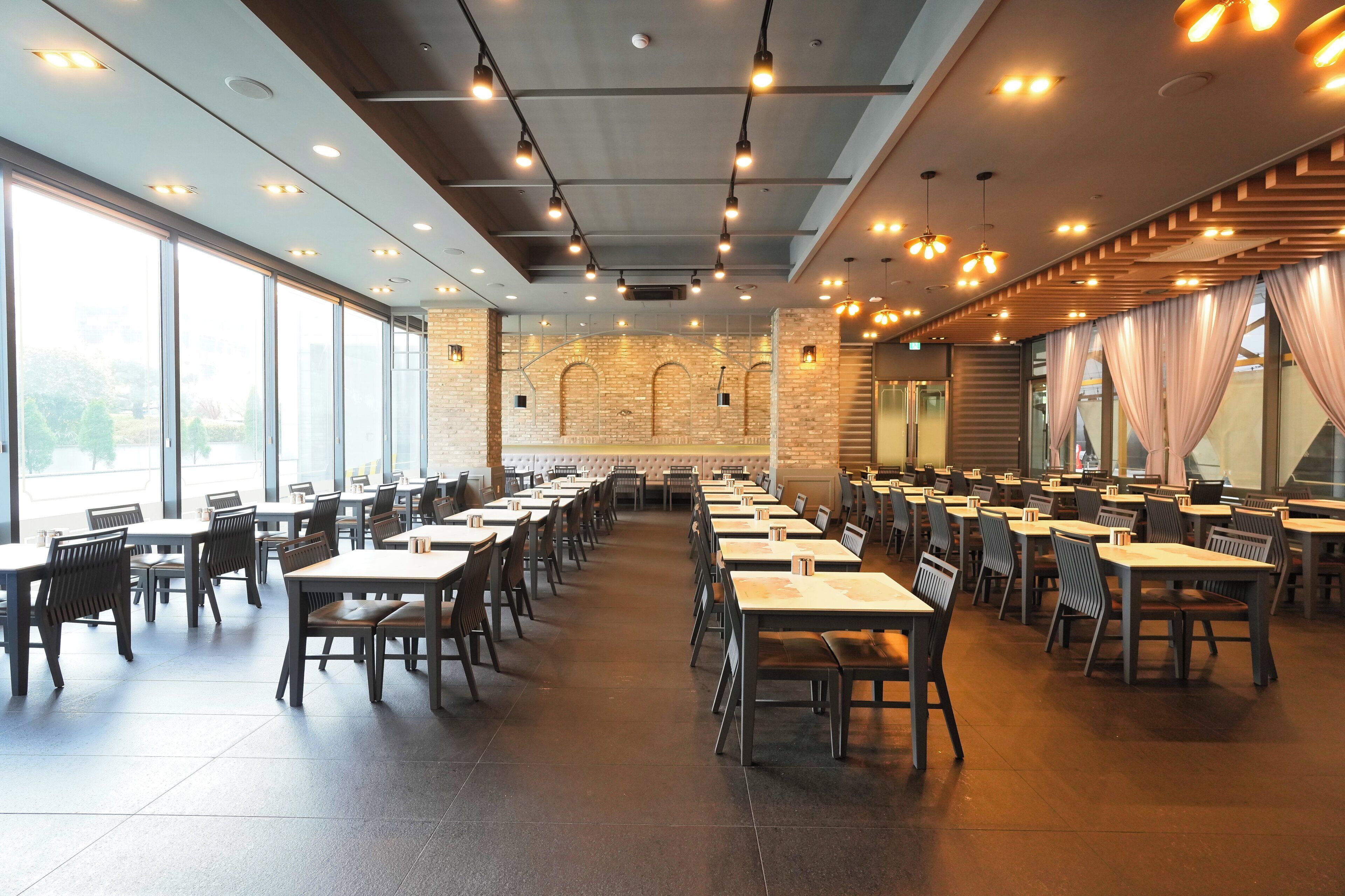 Een ruim restaurant met hoge plafonds, moderne verlichting en grote ramen.