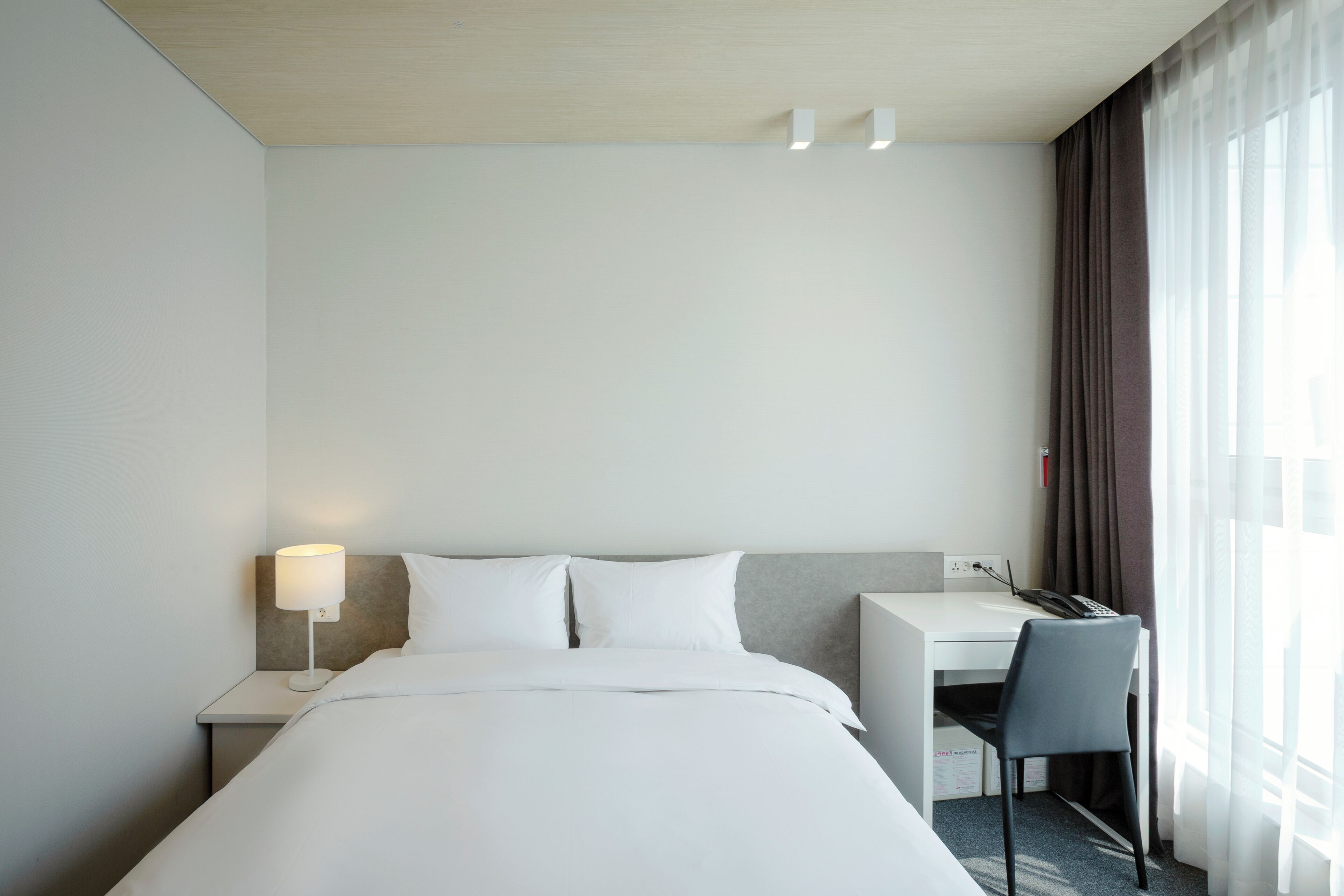 Una habitación de hotel con cama, escritorio, silla y lámpara.