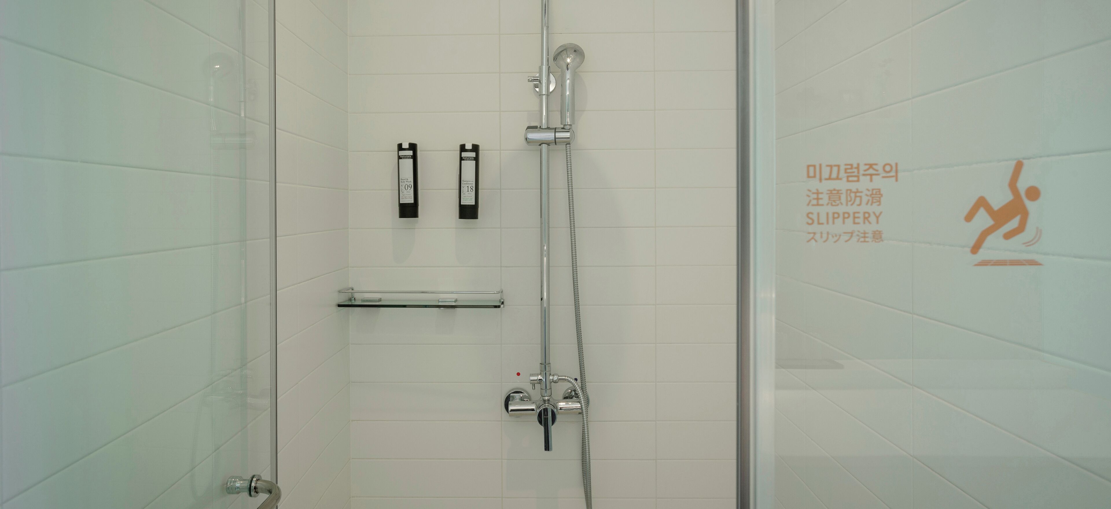 Un espace douche moderne doté d’une porte en verre, d’un pommeau de douche à main et de deux panneaux de commande.