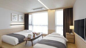 Habitación de hotel con dos camas, un escritorio, un televisor y una ventana con cortinas.