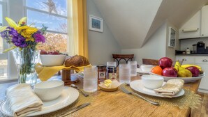 Una mesa de desayuno dispuesta con diversos alimentos, un jarrón de flores y vistas al exterior.