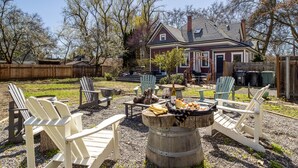 Un patio trasero con sillas Adirondack, un brasero y una casa al fondo.