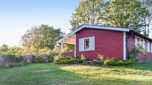 Ett rött hus med en veranda, omgivet av en gräsplätt och träd.